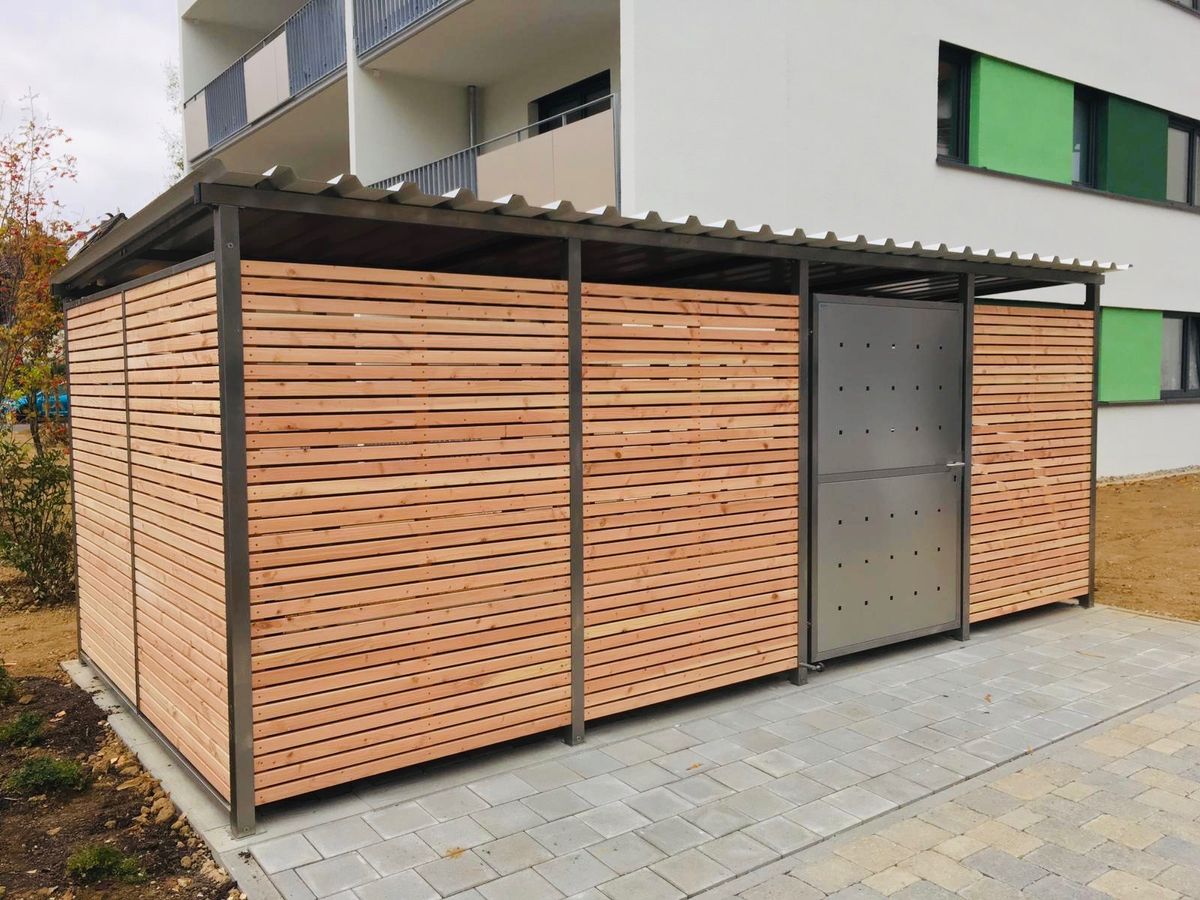 Mülltonnenhaus mit Lärchenholz-Verkleidung und Edelstahltür vor einer modernen Wohnanlage