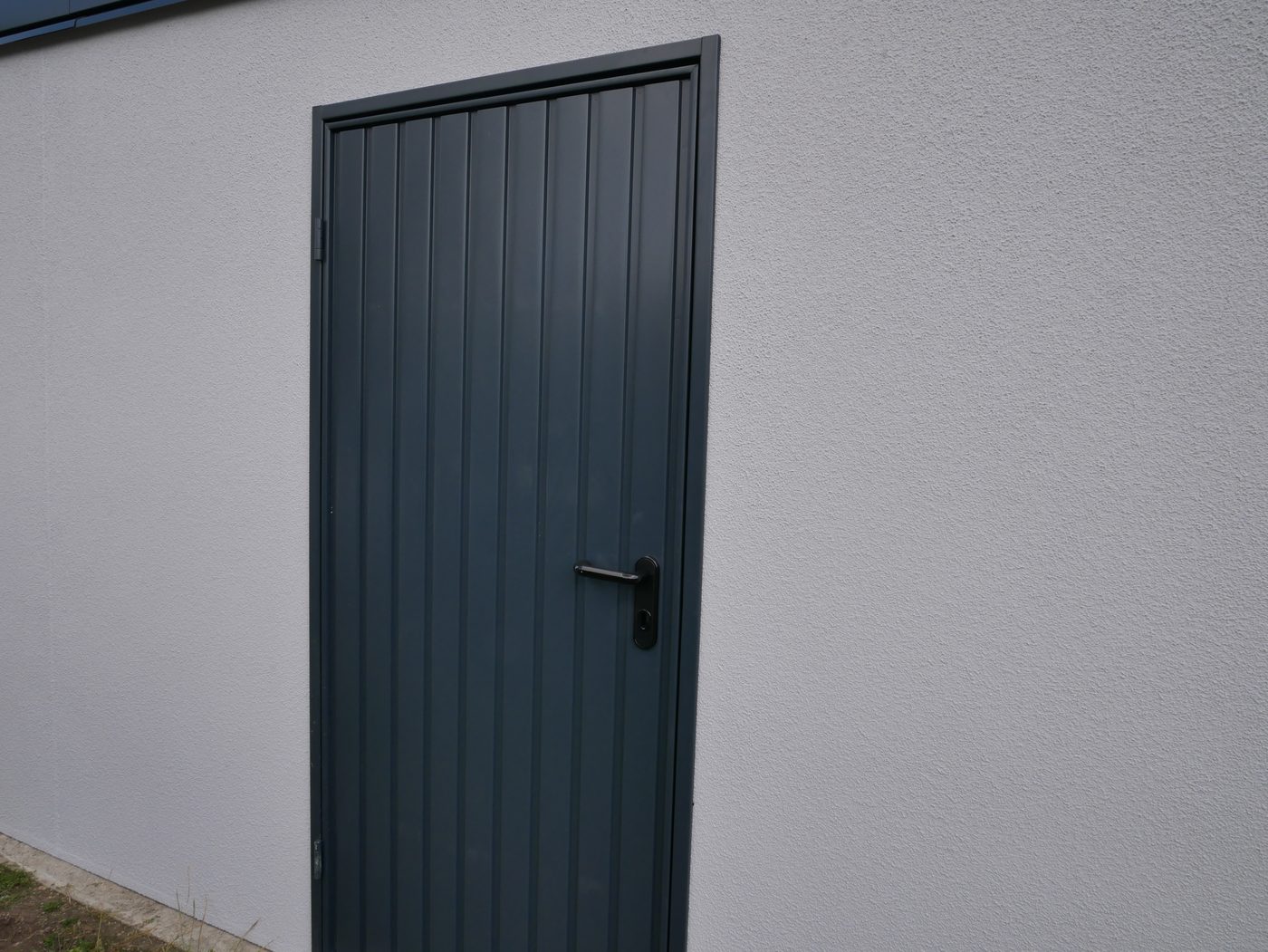 Anthrazitfarbene Nebentuer in der verputzten Wand einer Stahlgarage